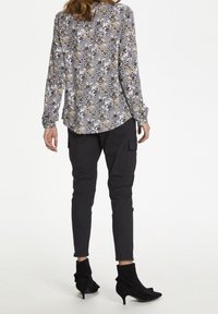 Blouse longue à manches longues à motifs floraux en blanc, noir, jaune et marron, associée à un pantalon cargo noir et des bottines noires avec des accents à volants.