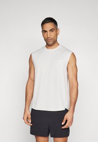Helles graues ärmelloses Sportshirt aus glattem Material, mit Rundhalsausschnitt und seitlichen Schlitzen, kombiniert mit dunklen Shorts.