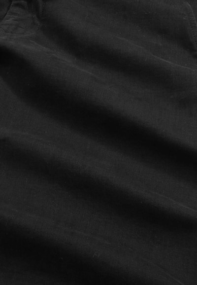 Schwarzer Stoff mit weichen Falten und sichtbarer diagonal verlaufender Webstruktur, die ein dezentes Muster über die Oberfläche bildet.