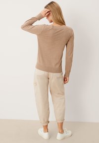 Maglione beige a maglia con maniche lunghe, polsini e orlo a coste. Abbinato a pantaloni cargo beige chiaro e sneakers bianche.