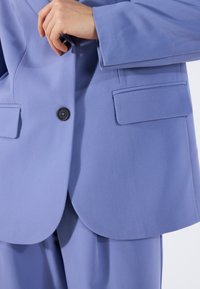 Lila blazer met een gladde textuur, een enkele zwarte knoop en twee voorkruiszakken; heeft een getailleerde pasvorm en een gebogen zoom.