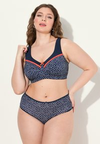 Navy blue-pinkki rintaliivejä ja korkeavyötäröisiä alushousuja, joissa on valkoisia ja punaisia pilkkuja. Ominaisuuksiin kuuluvat leveät olkaimet ja erottuva nauhadesign.