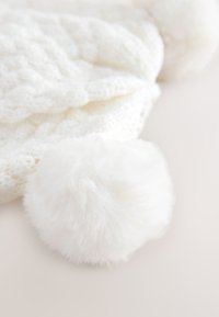 Cappello bianco lavorato a maglia con un motivo a trecce testurizzato, caratterizzato da un soffice pompon bianco in cima.