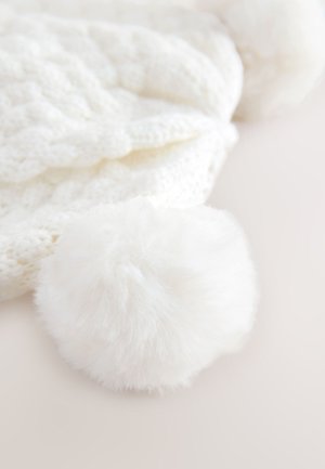 Gorro blanco de punto con un patrón trenzado texturizado y un suave pompón blanco esponjoso en la parte superior.