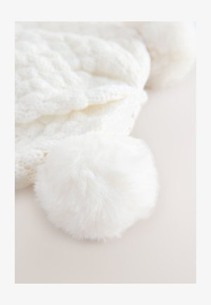 Valge kootud müts, millel on tekstuuriga palmikmustri ja pehme, kohev valge pom-pom otsas.