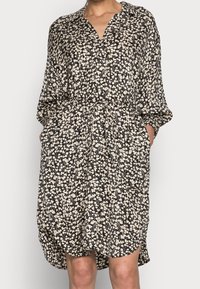 Schwarz-cremefarbiges Kleid mit Blumenmuster, aus leichtem Stoff gefertigt, verfügt über einen V-Ausschnitt, lange Ärmel, einen elastischen Taillenbund und seitliche Taschen.