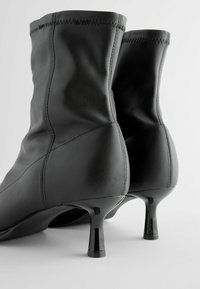 Bottines en cuir noir à design ajusté, avec des talons aiguilles brillants et des détails de couture visibles. Texture lisse et silhouette élégante.