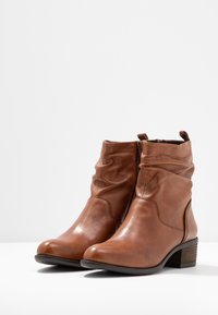 Ein Paar braune Leder-Stiefel mit niedrigen Blockabsätzen und seitlichen Reißverschlüssen auf weißer Oberfläche vor einfarbigem Hintergrund.