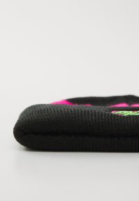 Chaussette noire en tricot, pliée avec une surface texturée, présentant des motifs géométriques roses et verts. Subtils côtes le long des bords.