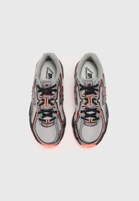Baskets de sport grises avec des lacets noirs et des accents orange. Matériau en mesh avec une languette rembourrée et des détails réfléchissants sur le côté.