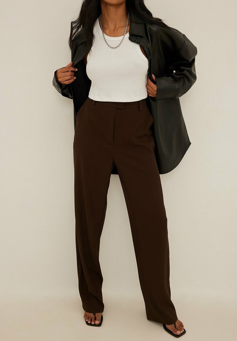 Höga bruna byxor kombinerade med en vit croppad tanktop och en svart oversized skjorta, med ett mjukt tyg och en avslappnad passform.