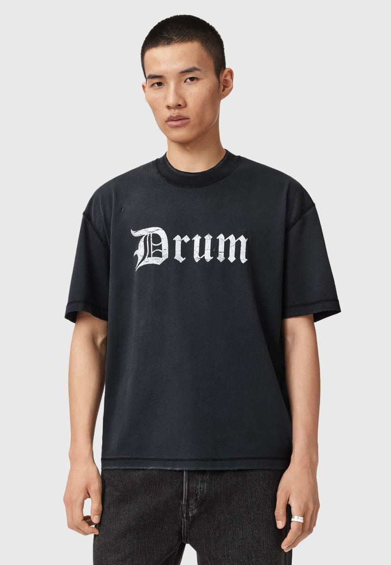 Czarny bawełniany T-shirt z dużym białym, gotyckim nadrukiem "Drum" na środku, krótkie rękawy i luźny krój.
