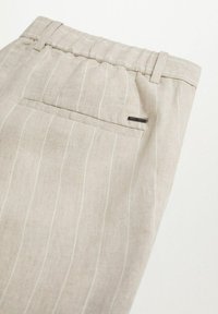 Pantalon en mélange de lin beige clair avec des fines rayures blanches, doté d'une ceinture élastique et d'une poche arrière avec une petite étiquette de marque.