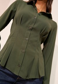 Cămașă cu nasturi verde măsliniu, cu talie ajustată, mâneci lungi și design plisat. Prezintă nasturi închiși la culoare și textură fină a țesăturii.