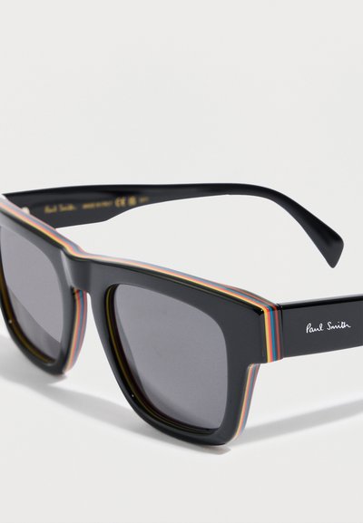 Μαύρα γυαλιά ηλίου με τετράγωνα πλαίσια και πολύχρωμες ρίγες γύρω από τα πλαίσια, με σκουρόχρωνους φακούς. Διαθέτουν ασημένιο λογότυπο "Paul Smith" στο μπράτσο.