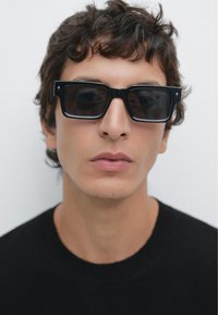 Czarne prostokątne okulary przeciwsłoneczne z ciemnymi szkłami, z błyszczącym wykończeniem i subtelnymi akcentami w kształcie gwiazdek na brzegach oprawki.