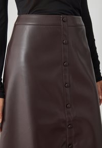 Falda de cuero sintético marrón con cintura alta, cierre frontal de botones con botones espaciados uniformemente y una textura suave y elegante.