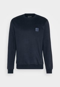 Sweat-shirt bleu marine à manches longues avec col rond, poignets et ourlet côtelés, affichant un petit patch de la marque sur la poitrine gauche.