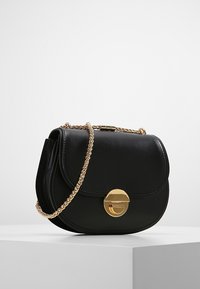 Musta nahkainen käsilaukku, jossa pyöreä muoto, kultainen ketjuhihna ja pyöreä magneettinen lukko. Sileä pinta ilman näkyviä kuvioita.