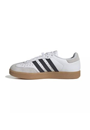 Witte sneaker met zwarte strepen, grijze suède neus en hiel, en een zool van natuurrubber, getoond in zijprofiel op een witte achtergrond.