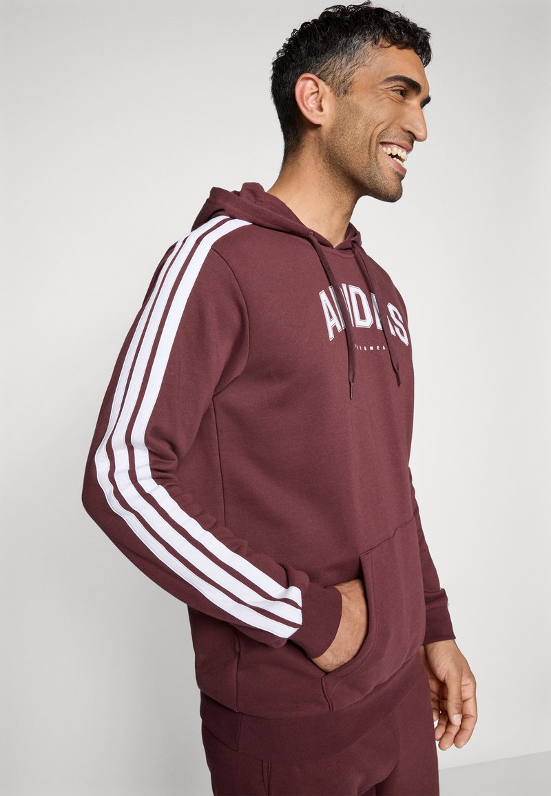 Hoodie bordeaux avec logo blanc et rayures verticales. Équipé d'une poche kangourou et d'une capuche à cordon de serrage réglable. Tissu en mélange de coton doux.