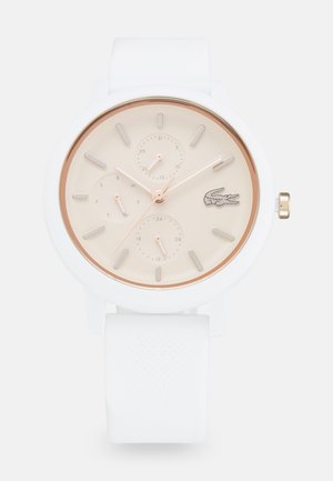 Montre en silicone blanche avec un cadran rond en rose doré, cadran crème, trois sous-cadrans et un logo crocodile ; elle dispose d'index et aiguilles luminescents.