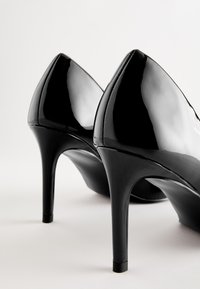 Zwarte lakleren hoge hakken met een puntige neus, strak ontwerp en smalle stilettohak. Voorzien van een glanzende afwerking en subtiele stikdetails.