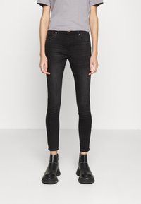 Jeans negros ajustados de mezclilla, con cinco bolsillos, cierre de botón y diseño minimalista. Llevados con botas negras hasta el tobillo.