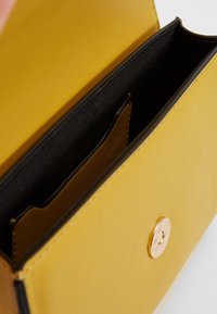 Interno di una borsa in pelle gialla con foderatura nera, un slot per carte e una chiusura a bottoncino rotondo dorato.