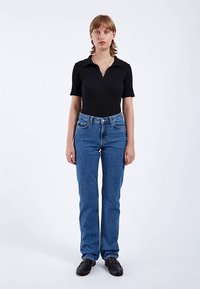 Svart ribbad kortärmad topp kombinerad med blå jeans med raka ben och svarta läderskor utan snören; minimalistisk design, enfärgade.