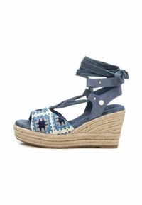 Sandalia de cuña con parte superior de textil azul, correas de ganchillo multicolores y suela de yute natural. Presenta cintas para el tobillo y detalles decorativos.
