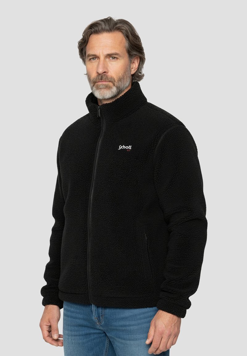 Schwarze Fleecejacke mit hohem Kragen, Frontreißverschluss und Seitentaschen; mit einem Schott-Logo auf der linken Brustseite.