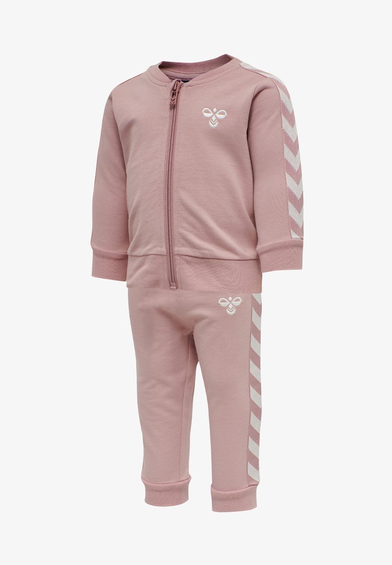 Różowa bluza z zamkiem i pasujące spodnie wykonane z miękkiego materiału. Posiada białe akcenty w kształcie zygzaka na rękawach i bokach spodni oraz detale z logo.
