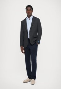 Blazer gri cu rever tip notch, cămașă cu dungi albastre și albe, pantaloni bleumarin și loafers de culoare deschisă. Blazerul are un accent albastru la mansetă.
