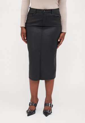 Mujer con falda de cuero negra hasta la rodilla, camiseta beige de manga larga y zapatos negros puntiagudos con hebillas plateadas.