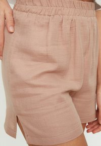 Shorts in lino rosa chiaro con vita elastica, fessure laterali e una vestibilità comoda. Il tessuto ha una finitura testurizzata.