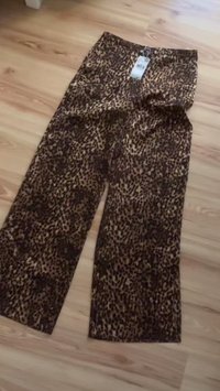 Pantalon à jambes larges imprimé léopard en marron et noir, fabriqué en tissu léger, avec une étiquette visible attachée à la taille.