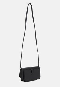 Černá crossbody taška vyrobená z hladkého materiálu má překlopný klopový uzávěr, štíhlý design a nastavitelného dlouhého popruhu.