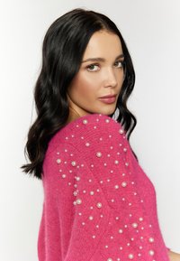Maglione rosa brillante realizzato in tessuto morbido, caratterizzato da dettagli in perle lungo le spalle. Il design è comodo con scollo rotondo.