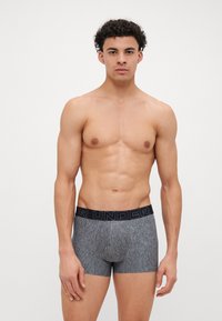 Bóxer gris con una cinturilla negra que presenta el texto "YOUR UNDER". Hecho de una tela texturizada, ofrece un ajuste ceñido.