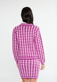 Stickad klänning i rosa och vit hundtandsmönster, med ribbad krage och ärmslut, figurnära design och texturerad tyg.