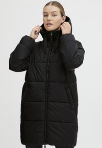 Svart pufferjakke med hette, med glidelås foran, elastiske mansjetter og en quiltet design. Materialet ser glatt og isolert ut.