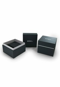 Des boîtes en carton noir avec une finition mate ; l'une d'elles est ouverte et révèle un intérieur gris. Toutes les boîtes portent le logo "BREIL" en texte blanc.