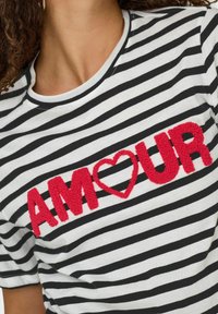 Korte mouwen gestreepte t-shirt in zwart en wit met een textuur ontwerp van een rode "AMOUR" en een hart op de borst. Ronde hals.