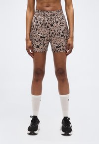 Άτομο που φοράει σορτς μπεζ με μαύρες βούλες, λευκές κάλτσες μέχρι τον αστράγαλο και μαύρα αθλητικά παπούτσια, στέκεται μπροστά σε ένα απλό φωτεινό φόντο.