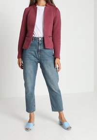 Bordeaux texturerad blazer med ståkrage, kombinerad med högmidjade ljusblå jeans och ljusblå öppna klackskor.