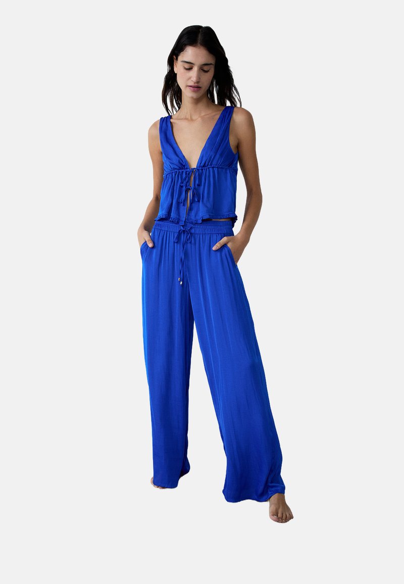 Ensemble deux pièces bleu comprenant un crop top à décolleté en V profond avec un détail à nouer et un pantalon ample avec une taille élastique et des poches.