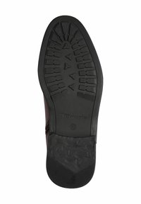 Semelle de chaussure en caoutchouc noir avec un motif de semelle texturé et un logo en relief, présentant un talon légèrement surélevé et une forme profilée.