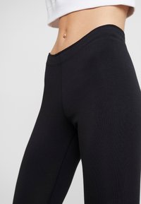 Svarta leggings gjorda av elastiskt material, med hög midja, sömlös design och slät textur, som sitter nära kroppen.