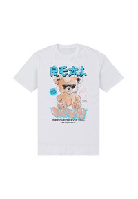 Bílý bavlněný tričko s potiskem karikatury medvěda v slunečních brýlích a barevným textem, který říká: "ROZTOMILÉ" a "SE VYVÍJÍ S ČASEM."